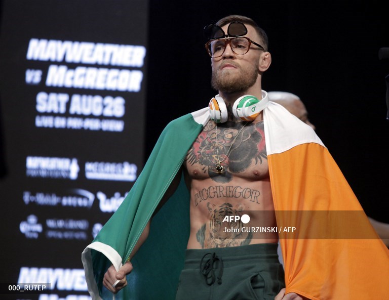 Petarung MMA Connor McGregor tiba di atas panggung terbungkus bendera Nasional Irlandia untuk penimbangan dengan petinju Floyd Mayweather Jr. pada 25 Agustus 2017 di T-Mobile Arena di Las Vegas, Nevada. 